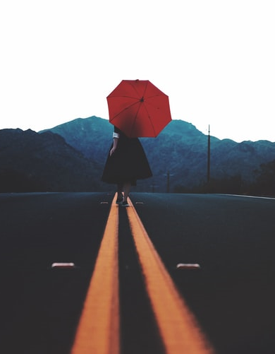 Doble línea continua naranja en una carretera sobre la que anda una mujer con paraguas