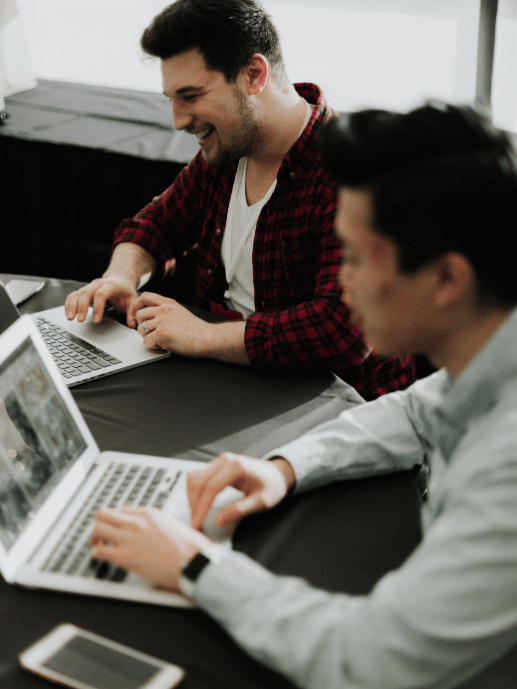 Dos hombres riéndose frente a sus portátiles