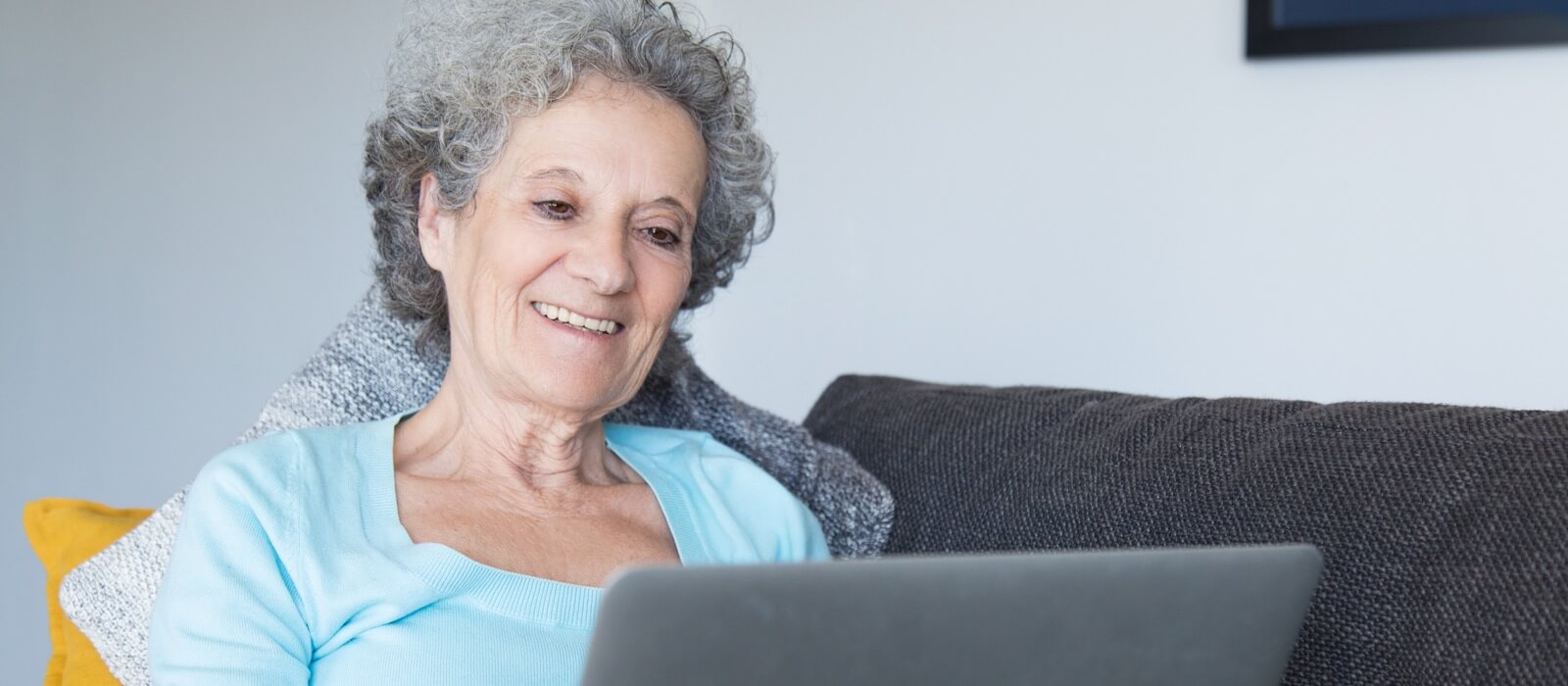 Babel Administración Electrónica Junta de Andalucia. Una anciana recostada en un sofá interactuando con un portátil