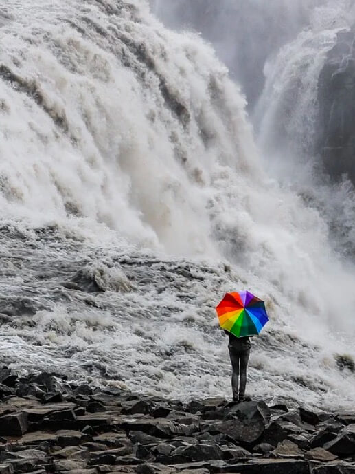 Babel Seguros. Hombre con un paraguas de colores al lado de una catarata